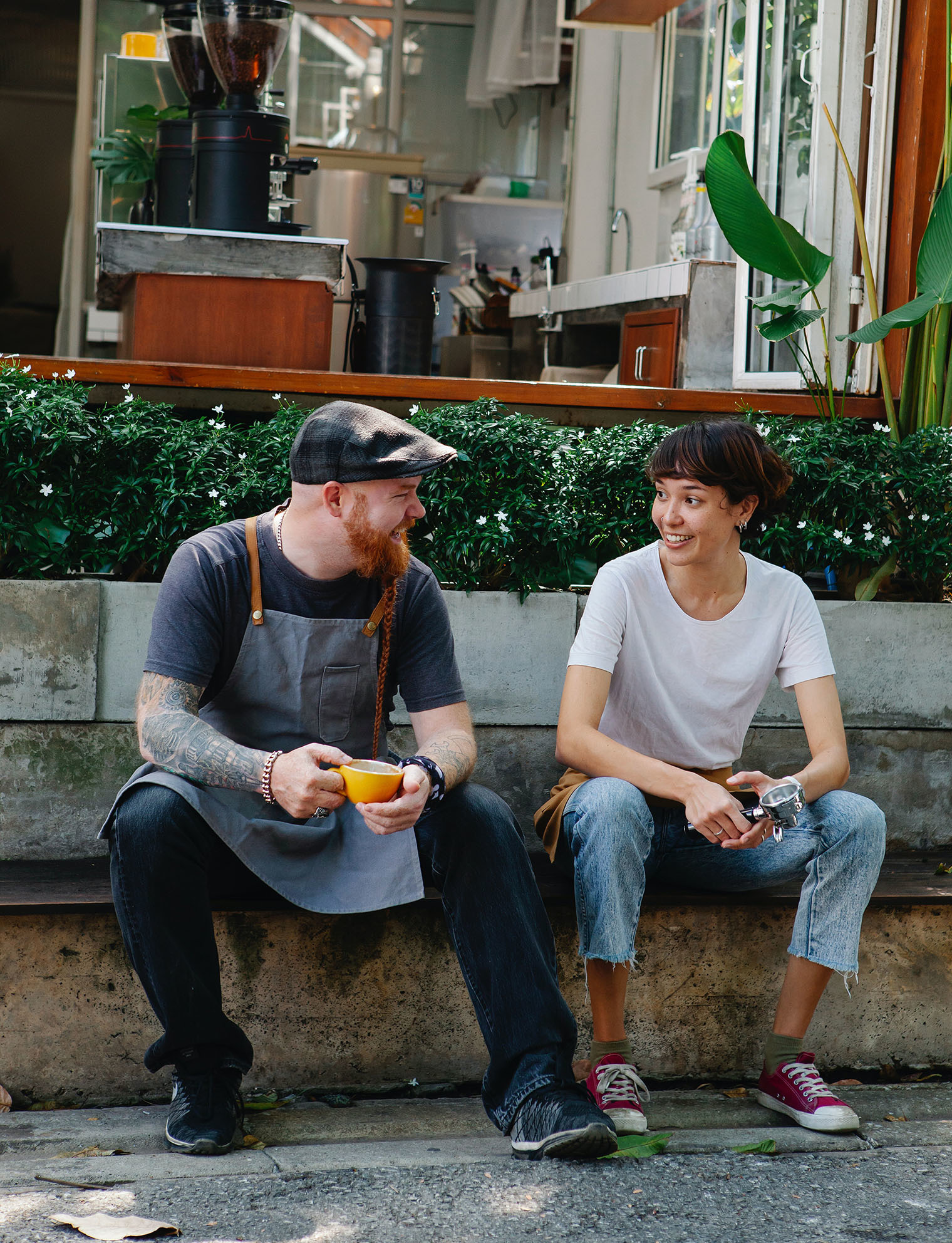 Zwei Kollegen in einem Café sitzen auf einer Bank, lächeln sich an und halten Kaffeetassen – ein Bild für Employer Branding, das die positive Teamatmosphäre und Zusammenarbeit zeigt.