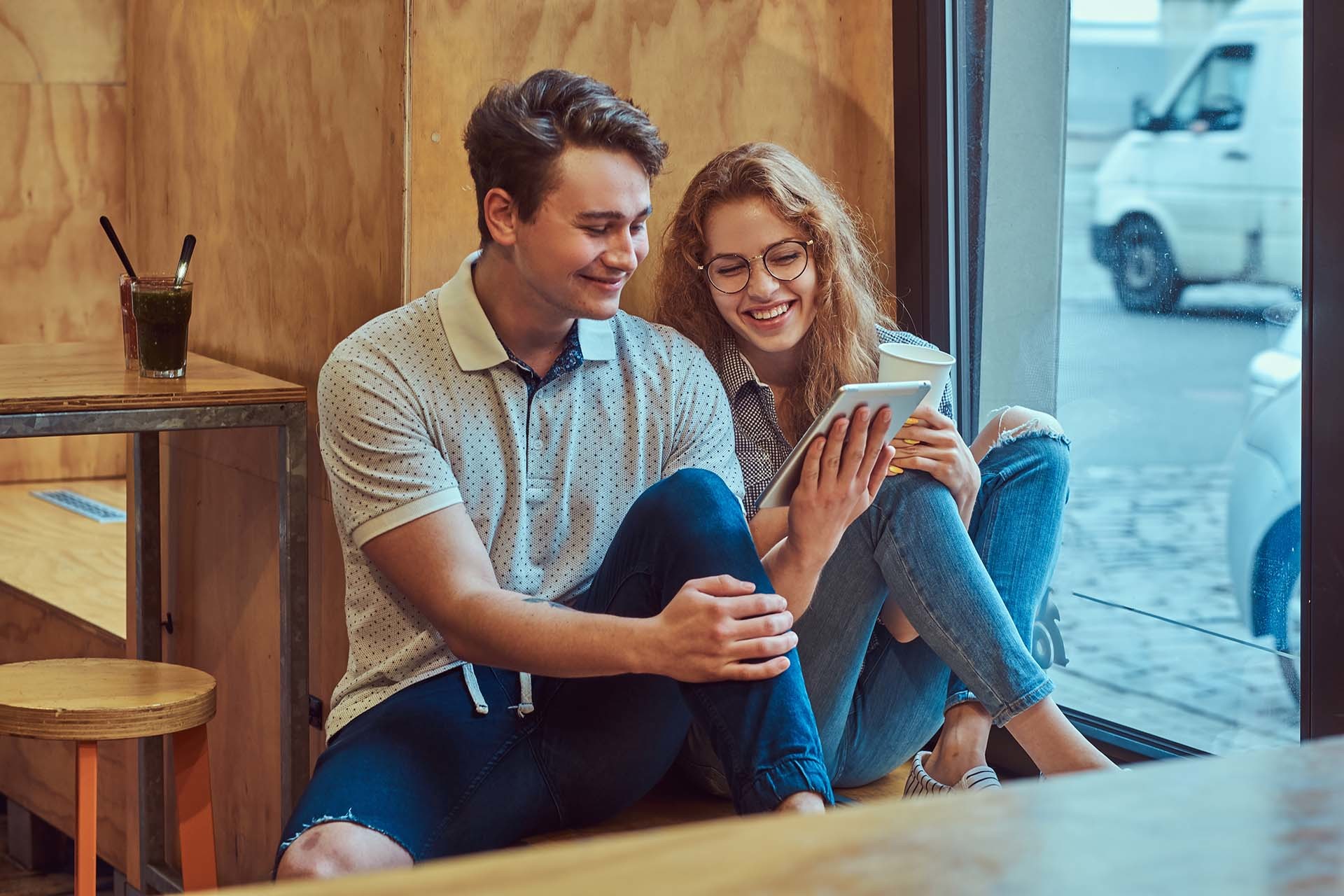 Zwei junge Menschen sitzen lächelnd in einem Café und betrachten gemeinsam ein Tablet – ein Bild für positive Teamdynamik und Kundeninteraktion in der Systemgastronomie, ideal für Employer Branding.