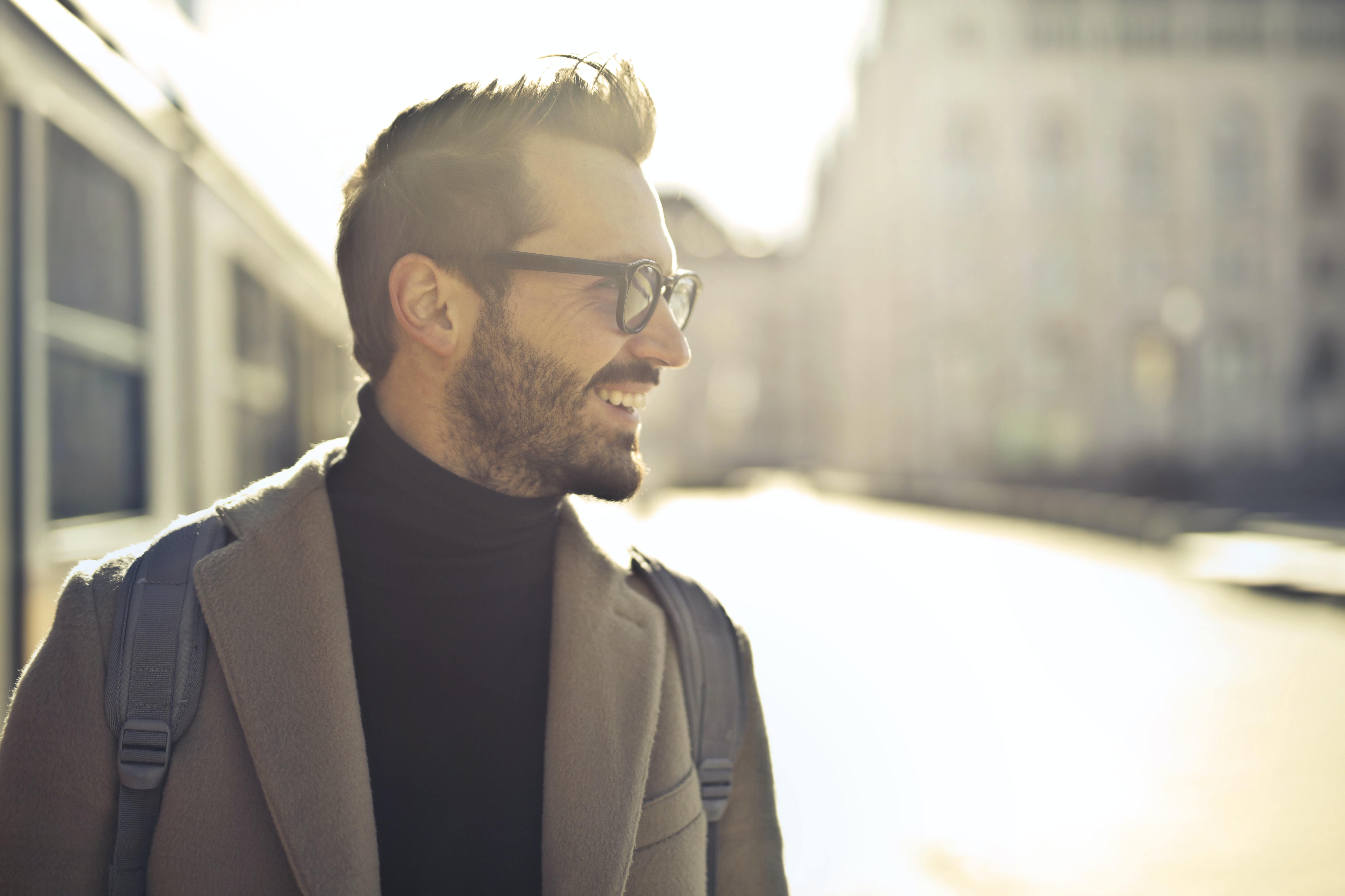 Lächelnder Mann in professioneller Kleidung (Brille, Mantel, Rucksack) in urbaner Umgebung – symbolisiert die klare, kreative Kommunikation, die N3W für Employer Branding und Markenstrategien bietet.